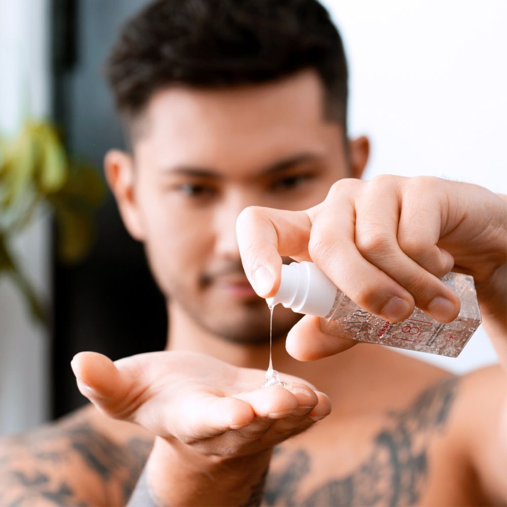 Man die SVR Aqua-Gel Sensifine op zijn hand aanbrengt. Transparante fles met witte pomp. Tatoeage op de arm.