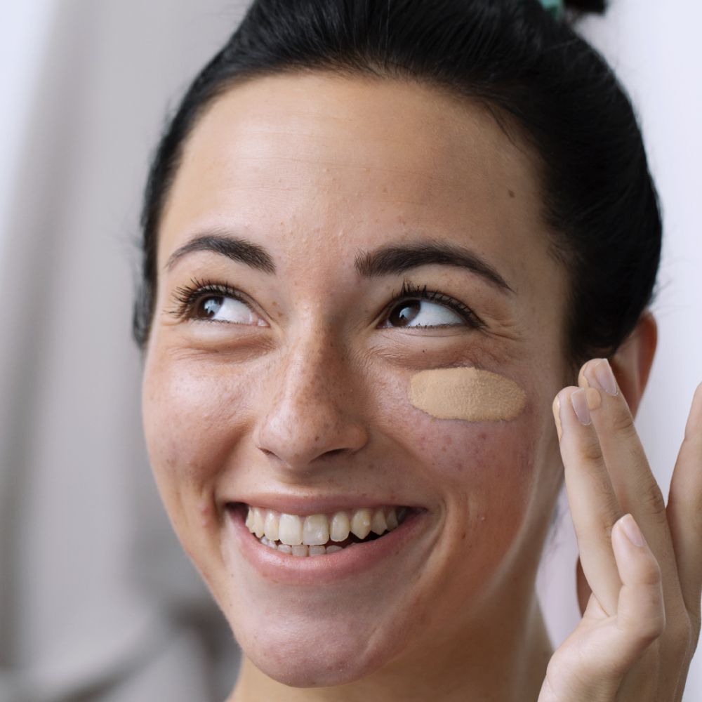 Femme appliquant SVR Sebiaclear Active Teinté sur son visage. Une zone du visage est couverte. Elle sourit.