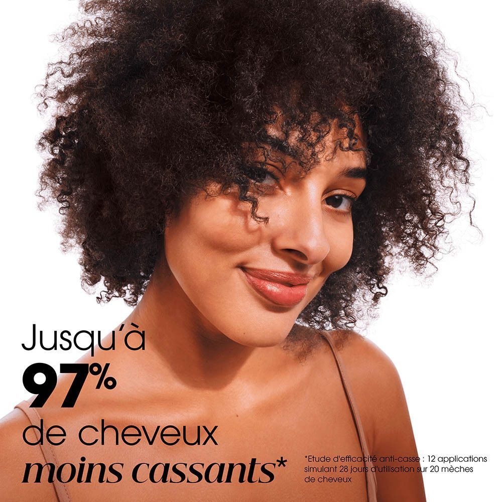 Femme souriante aux cheveux bouclés et volumineux. Texte : Jusqu'à 97% de cheveux moins cassants.