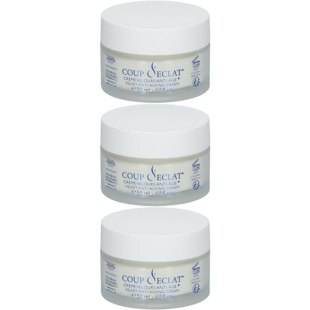 Trois pots de crème Coup d'Eclat® Crème Velours Anti-Âge. Pots blancs avec couvercles blancs. Inscription : Crème Velours Anti-Âge.