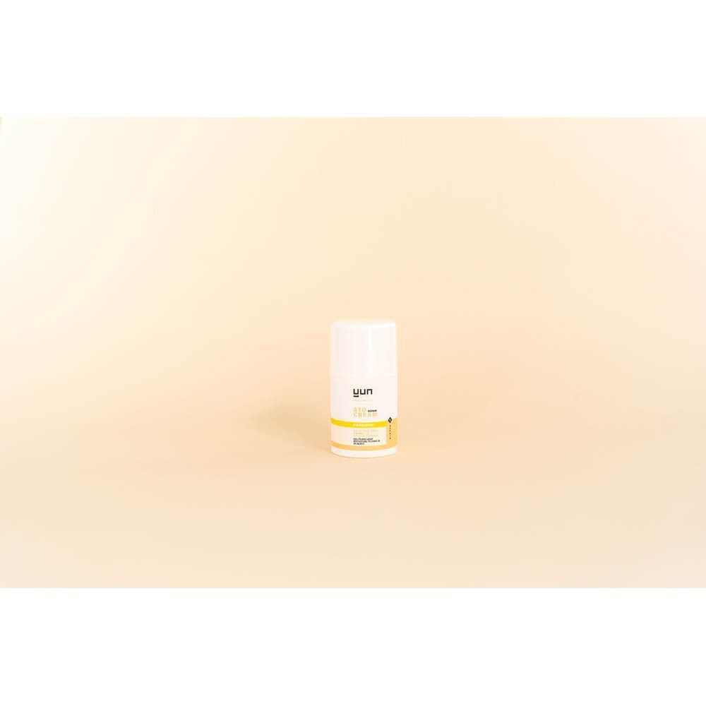 Een witte tube. Opschrift: YUN ATO CREAM. Gele en blauwe streep. Beige achtergrond.