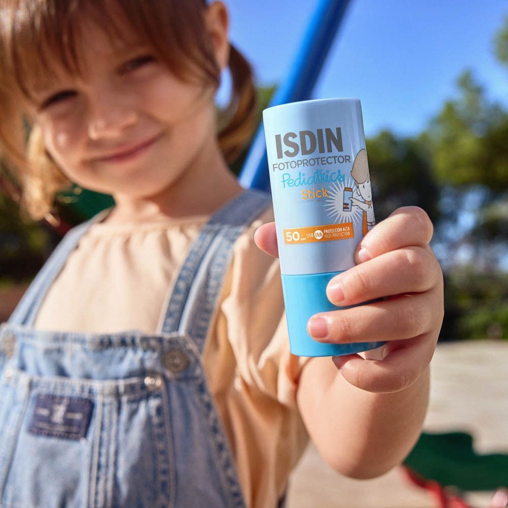 Kind houdt ISDIN Fotoprotector Pediatrics Stick vast. Blauw-witte tube, kind buiten.