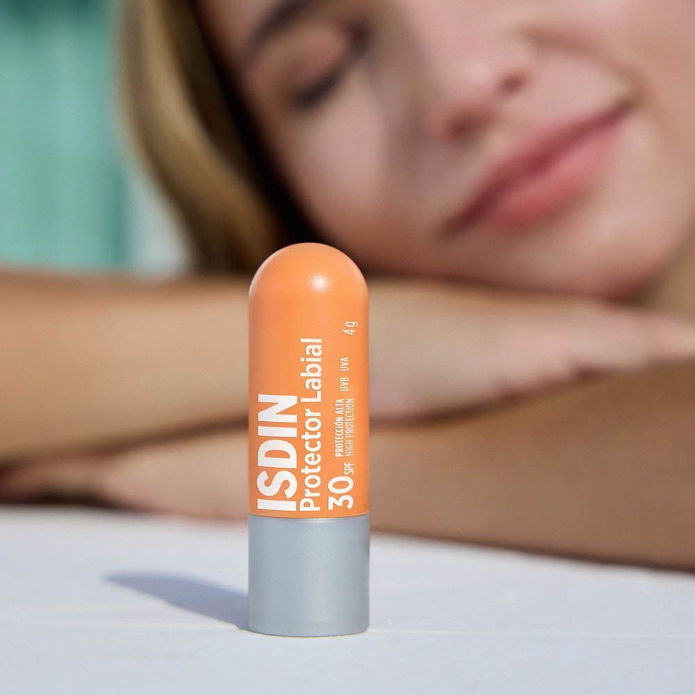 Lippenbalsemstift. Oranje kop, zilveren body. Opschrift: ISDIN Protector Labial 30. Persoon op de achtergrond.