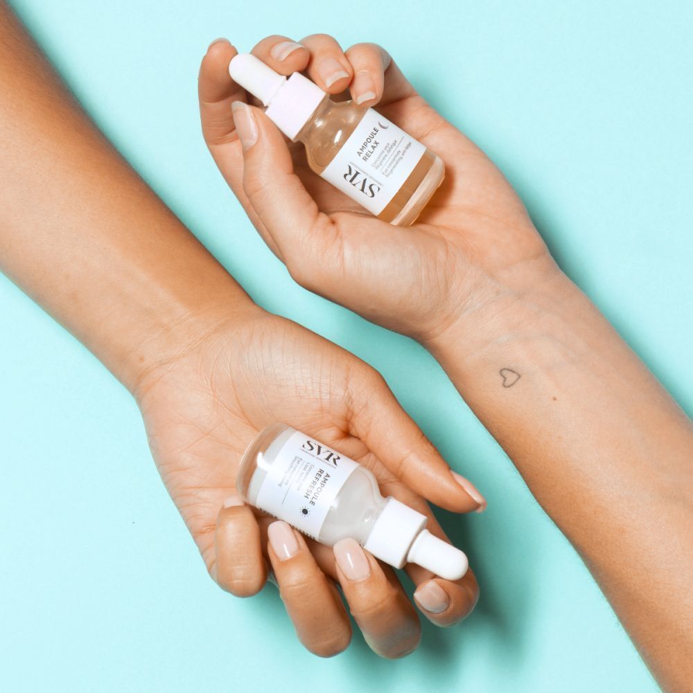 Twee kleine glazen flesjes met pipetten in handen. Flesjes met "SVR Ampoule Relax".