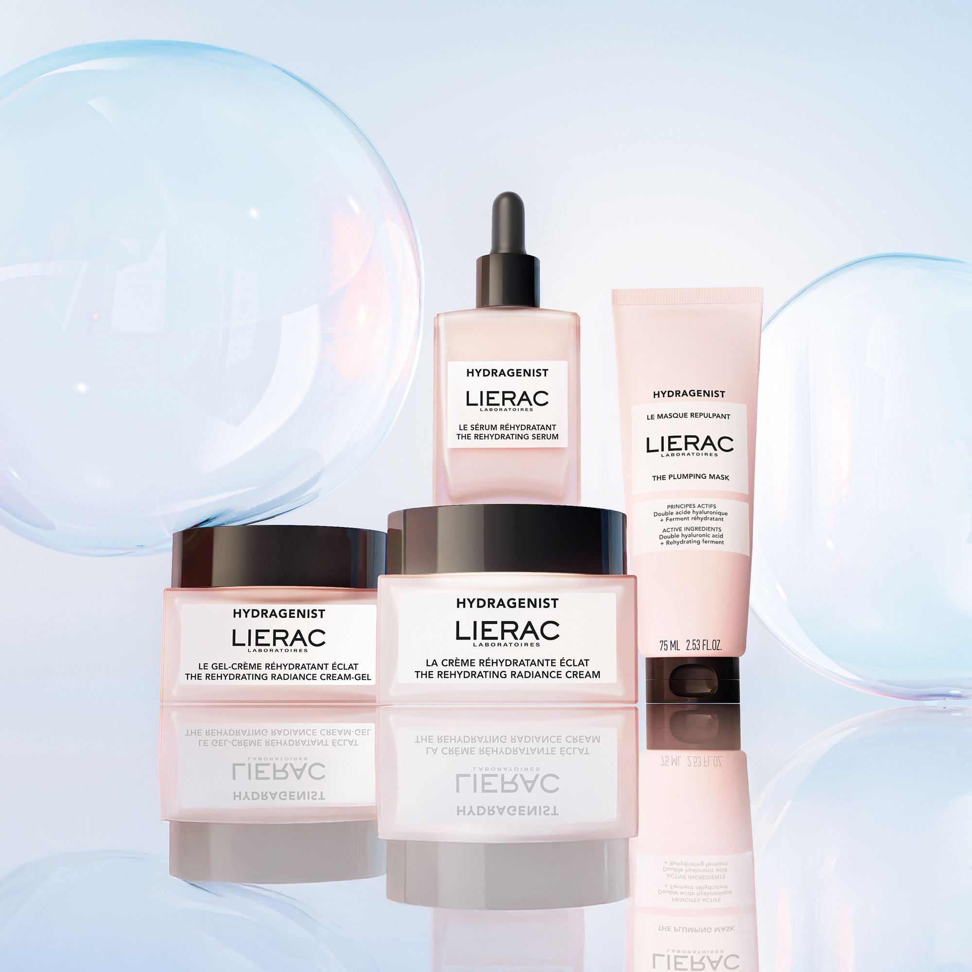 Plusieurs produits avec emballages roses. Inscription: HYDRAGENIST, LIERAC. Contient: sérum, crème, masque. Fond: bulles.