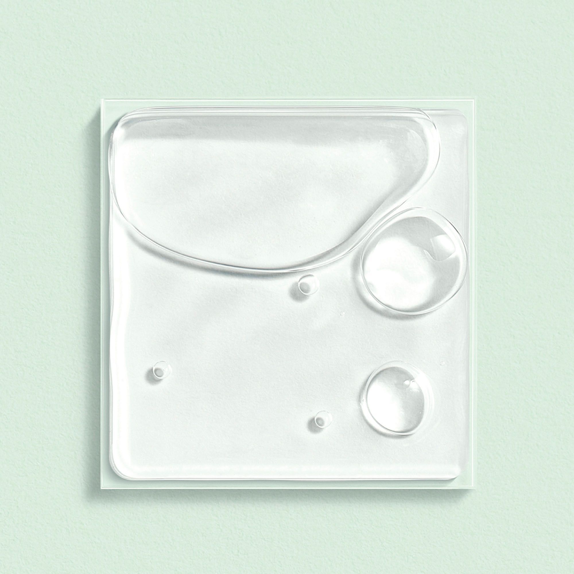 Liquide clair sur une surface carrée vert clair. Plusieurs gouttes et bulles.