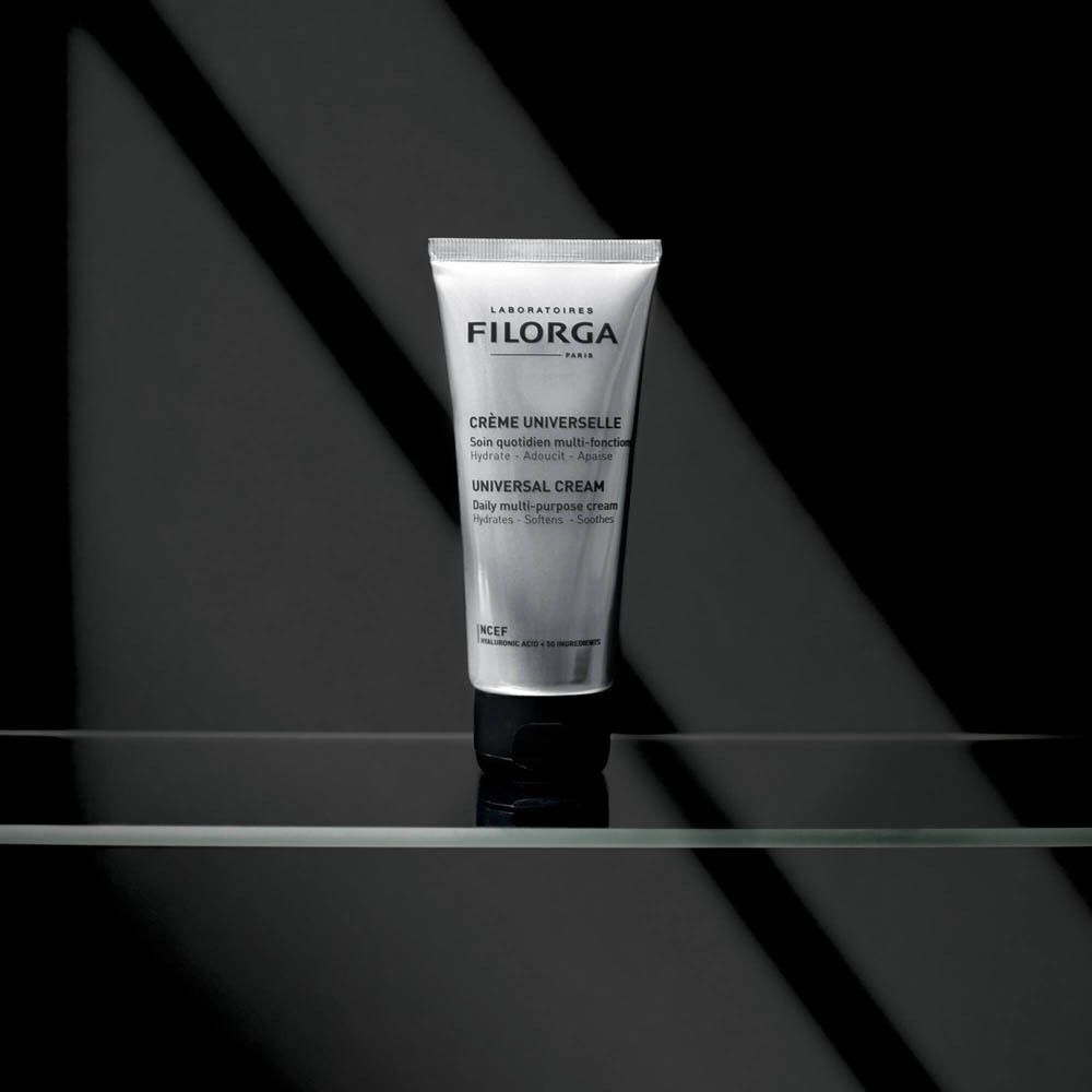 Tube Filorga CRÈME UNIVERSELLE sur une étagère en verre. Fond noir avec effets de lumière. Texte: CRÈME UNIVERSELLE, UNIVERSAL CREAM.
