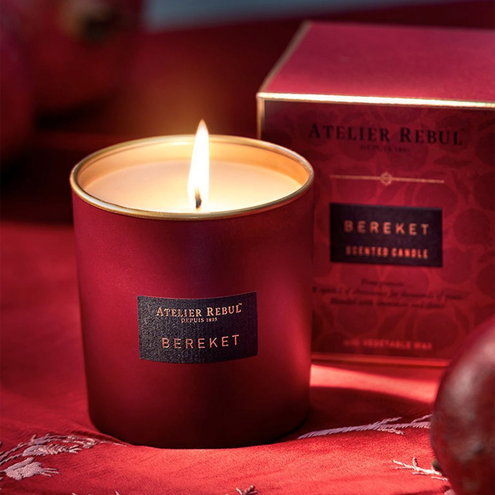 Bougie parfumée allumée dans un récipient en verre rouge à bord doré. Marque : Atelier Rebul, variété : Bereket.