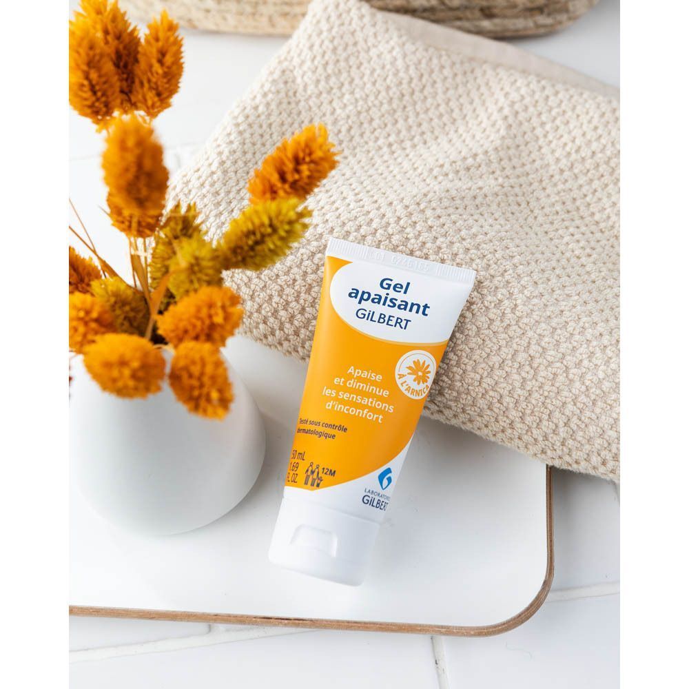 Un tube de Gel apaisant à l'arnica Gilbert sur une serviette, à côté d'un vase de fleurs.