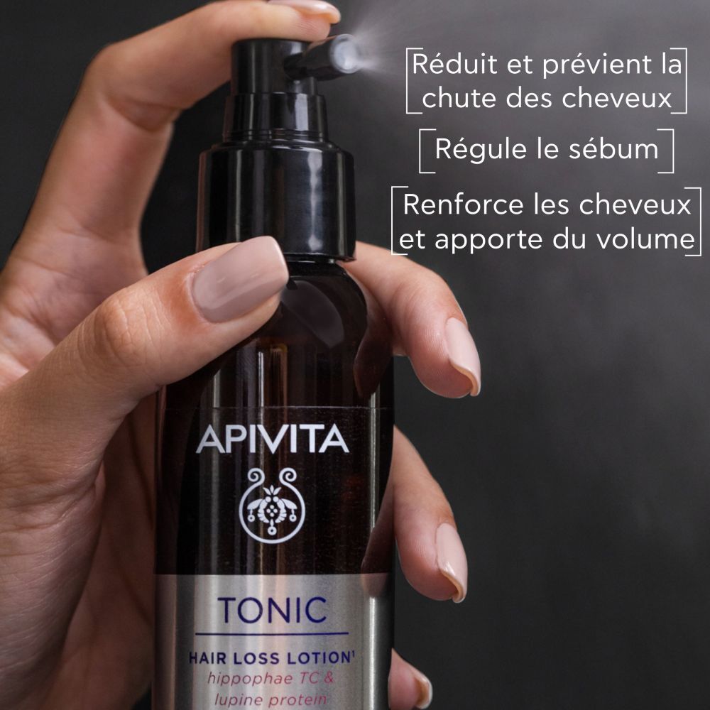 Main tenant la lotion Apivita Tonic. Texte : Réduit et prévient la chute des cheveux.