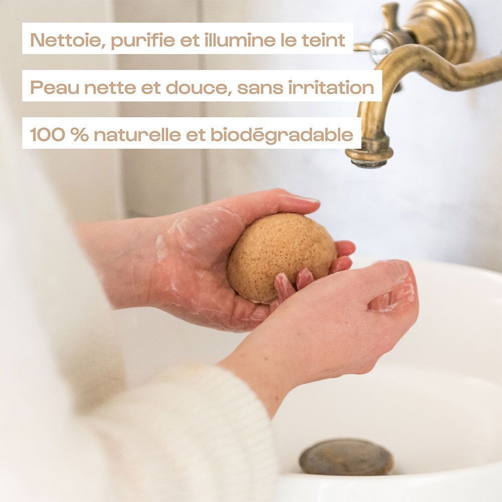Mains tenant une éponge Konjac Omum sous l'eau courante.