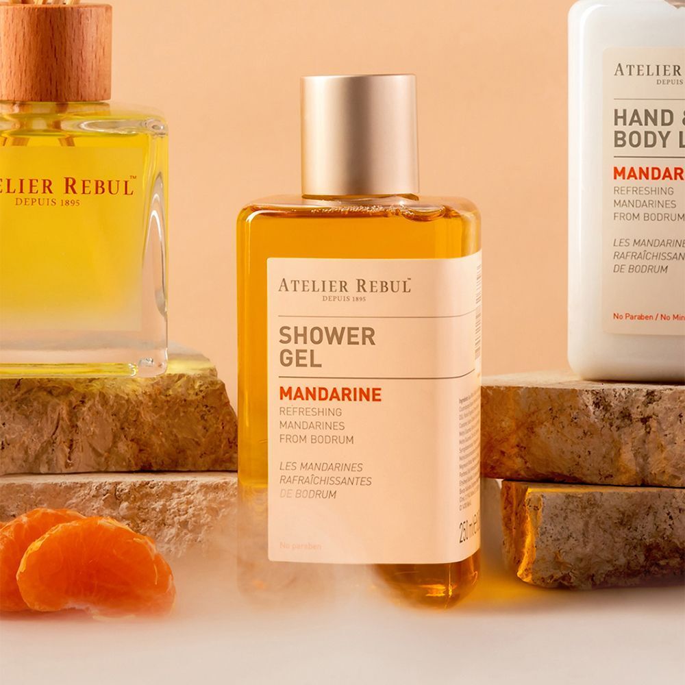 Twee flessen Atelier Rebul Mandarine hand- en bodylotion. Witte lotion in rechthoekige pompflesjes met gouden accenten.