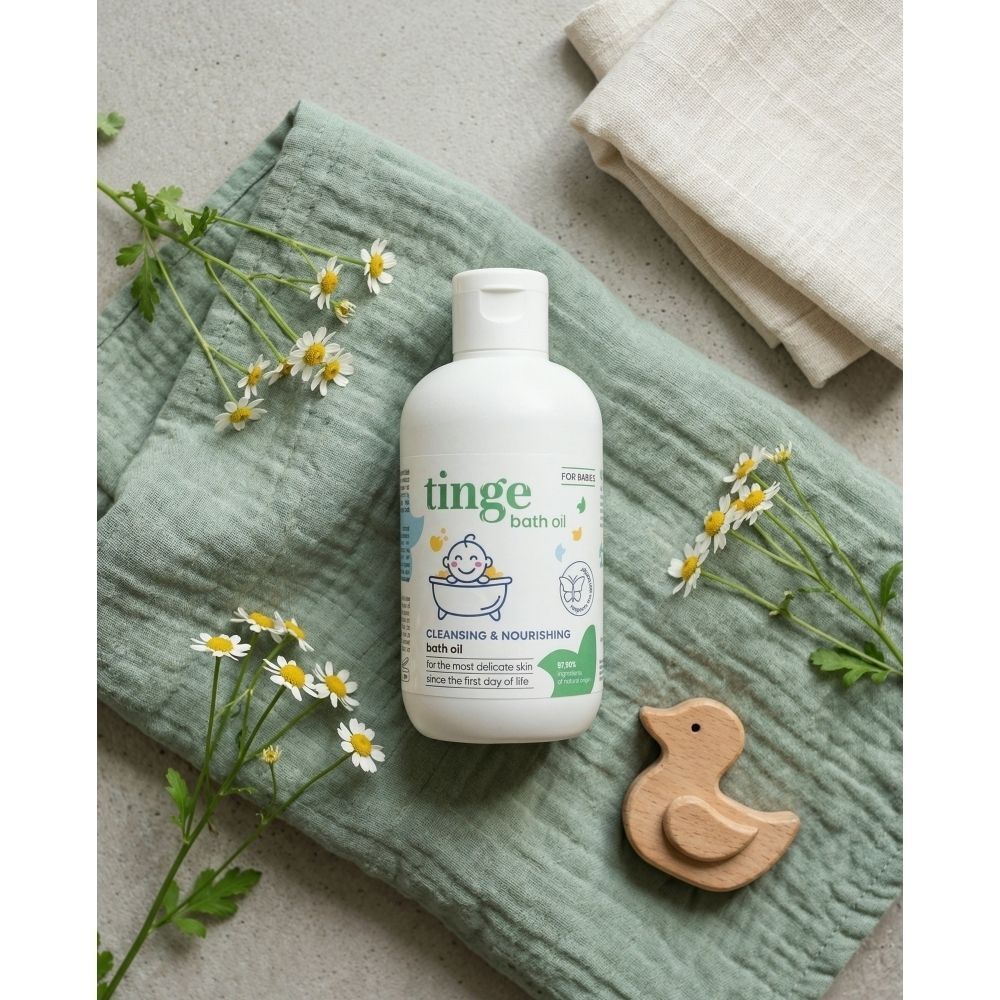 Een fles Tinge baby badolie op een groene doek, omringd door madeliefjes en een houten eendje.