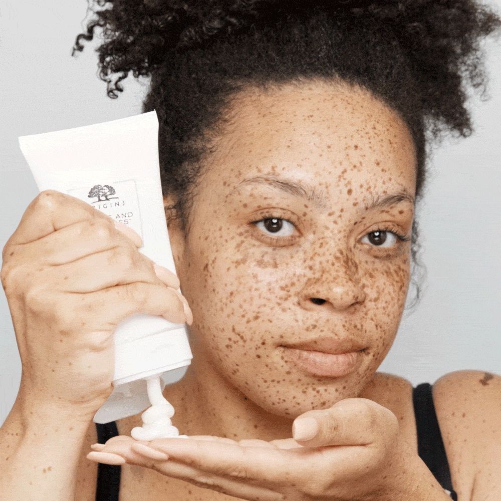 Femme aux taches de rousseur tenant un tube de nettoyant visage moussant ORIGINS Checks and Balances™.