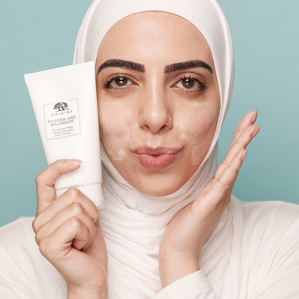 Femme portant un foulard tenant un tube de nettoyant visage ORIGINS Checks and Balances™.