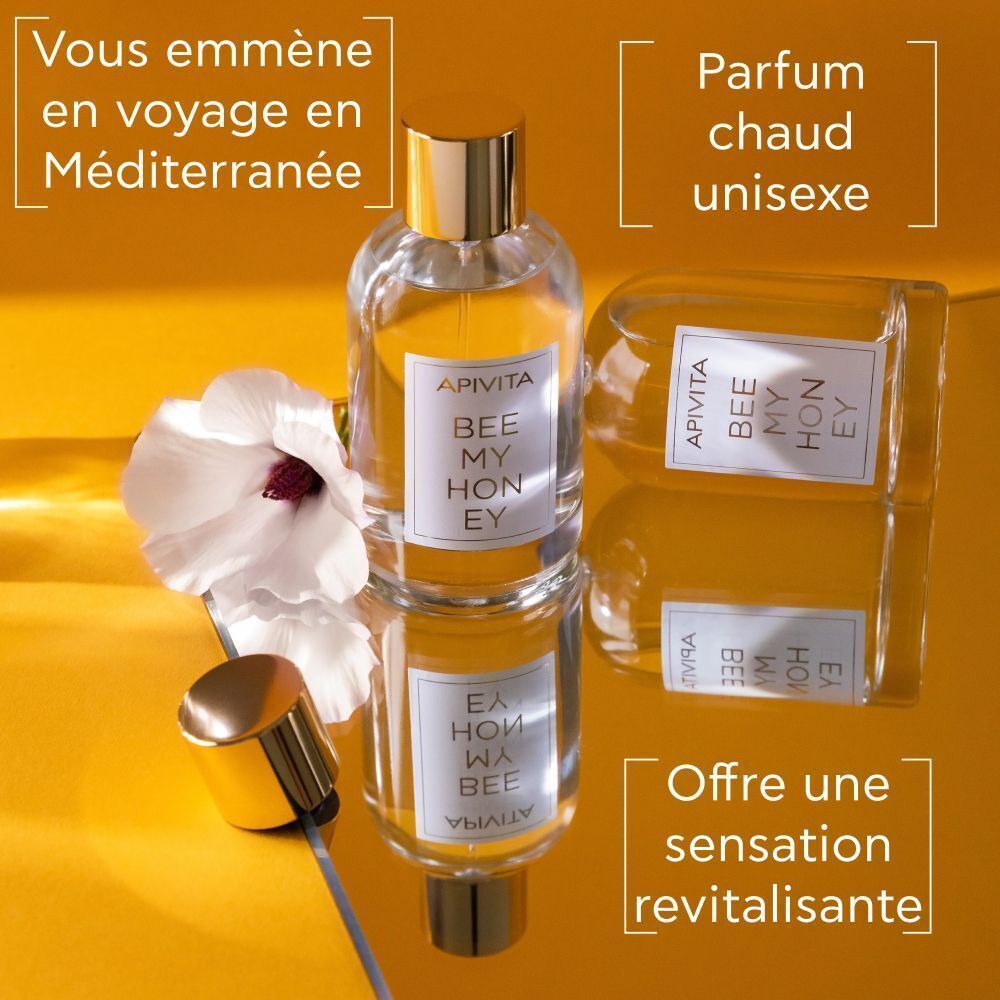 Apivita Bee My Honey Eau de Toilette : Un flacon et un flacon renversé sur une surface réfléchissante, avec une fleur.