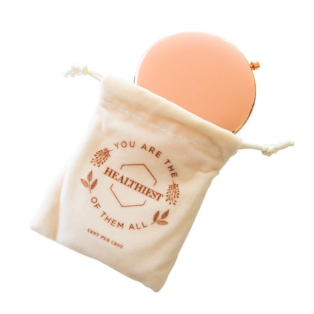 Miroir cosmétique rond en or rose, partiellement dans un sac crème à cordon de serrage.