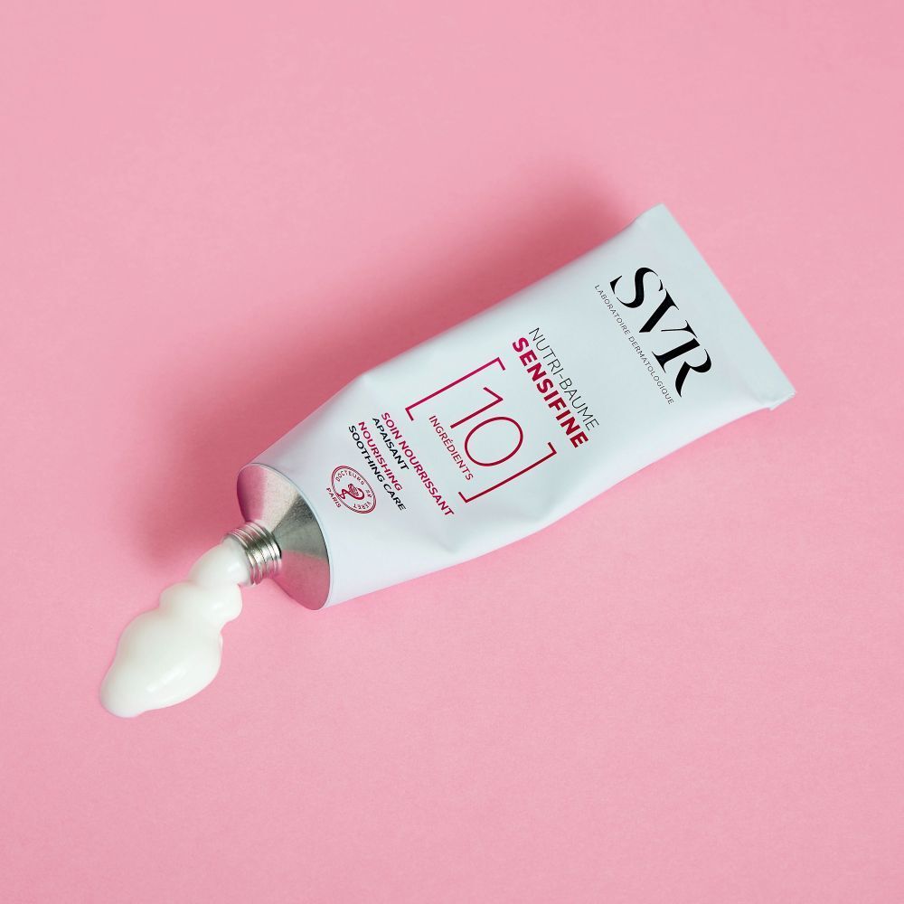 Un tube blanc SVR Sensifine Nutri-Baume posé sur fond rose, avec une trace de crème sortant de l'ouverture.