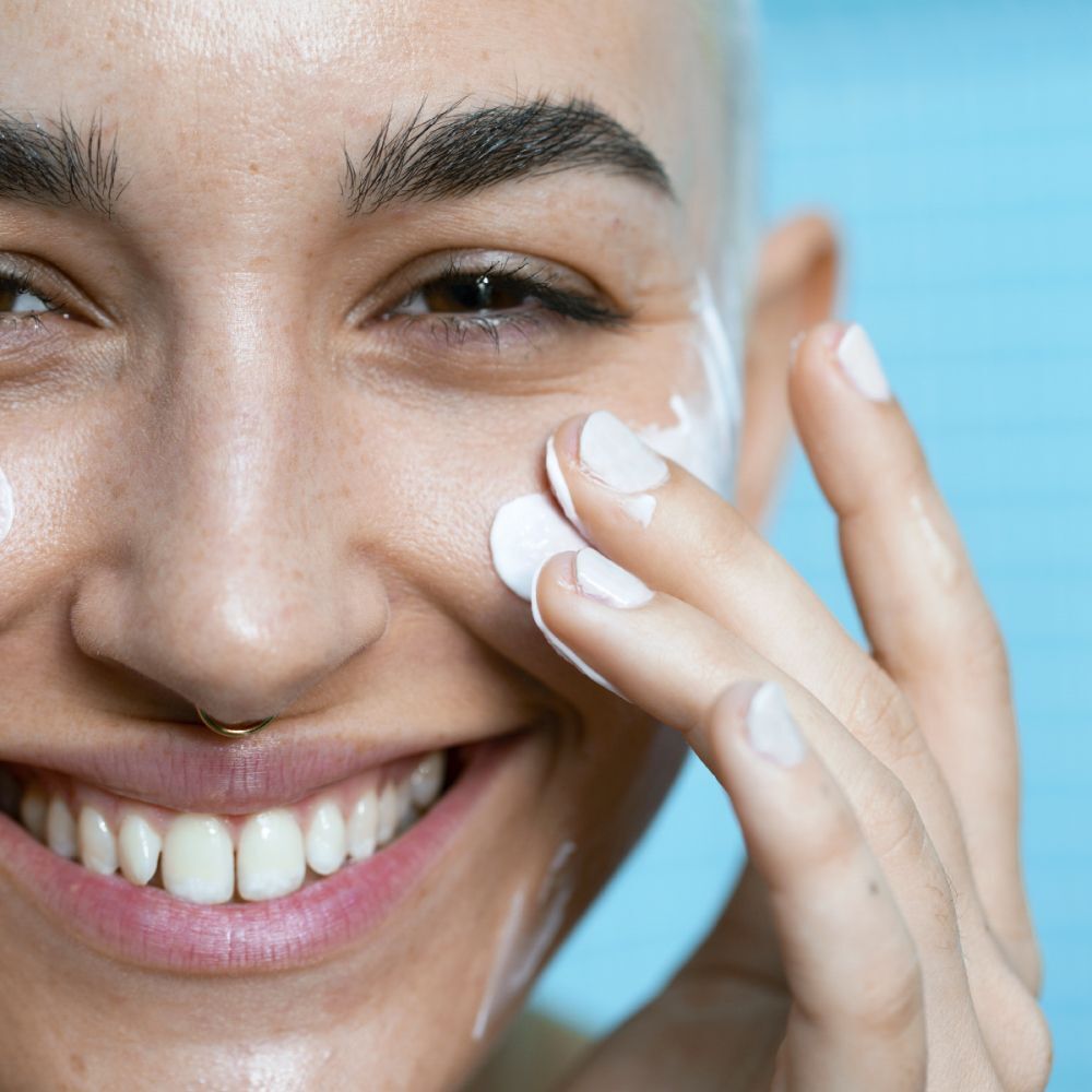 Gros plan d'un visage sur lequel une personne applique une crème blanche avec ses doigts. De la crème blanche est visible sur la peau.