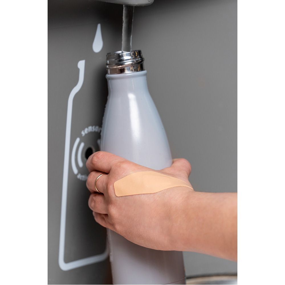 Een Nexcare Flexible Foam Active pleister op de hand van een persoon die drinkt.