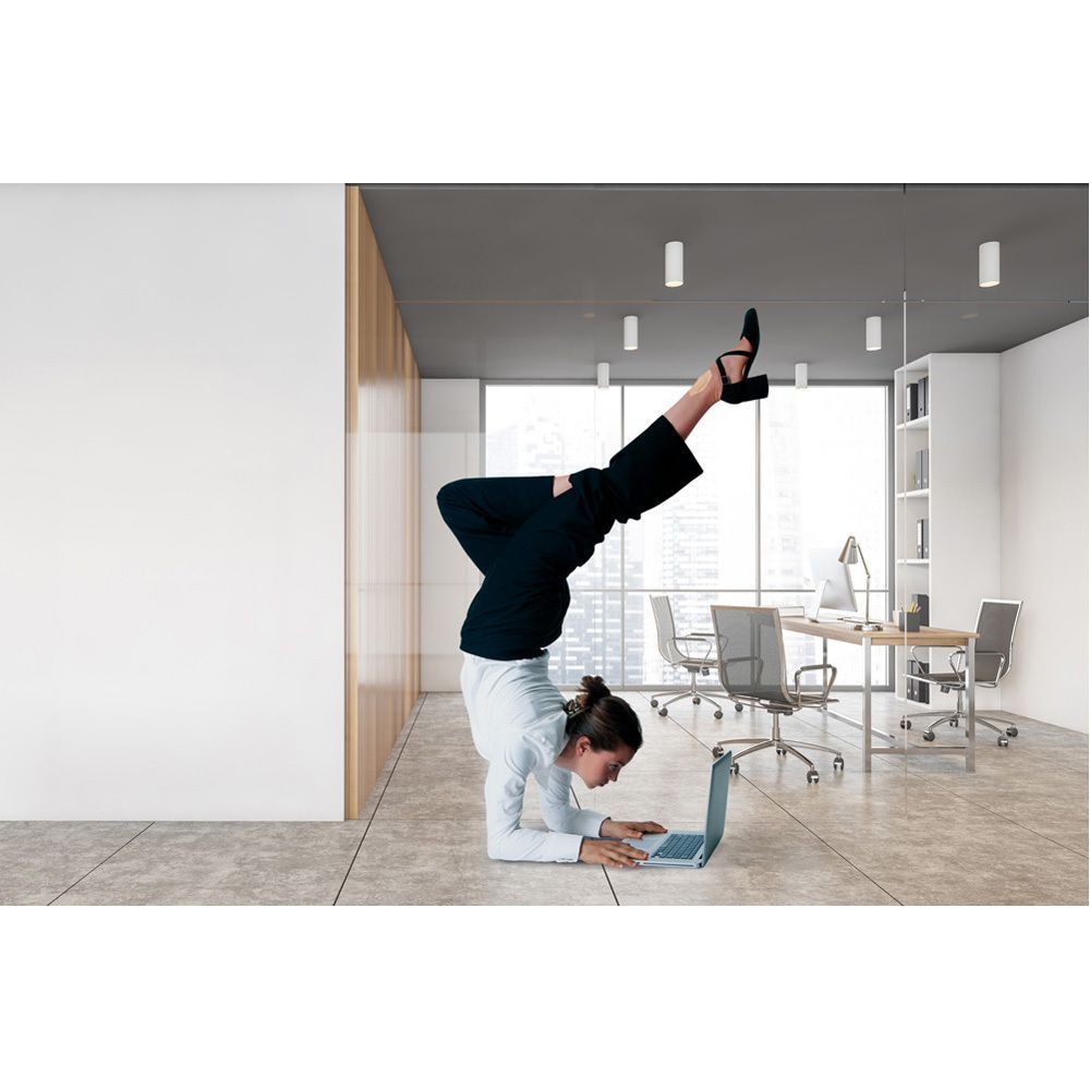Une femme fait une pose de yoga en équilibre sur les mains avec un ordinateur portable au bureau.