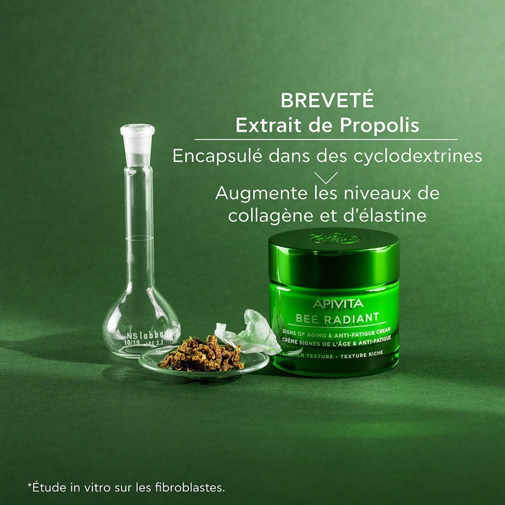 Un pot vert de crème Apivita Bee Radiant près d'équipement de laboratoire et d'extrait de propolis.