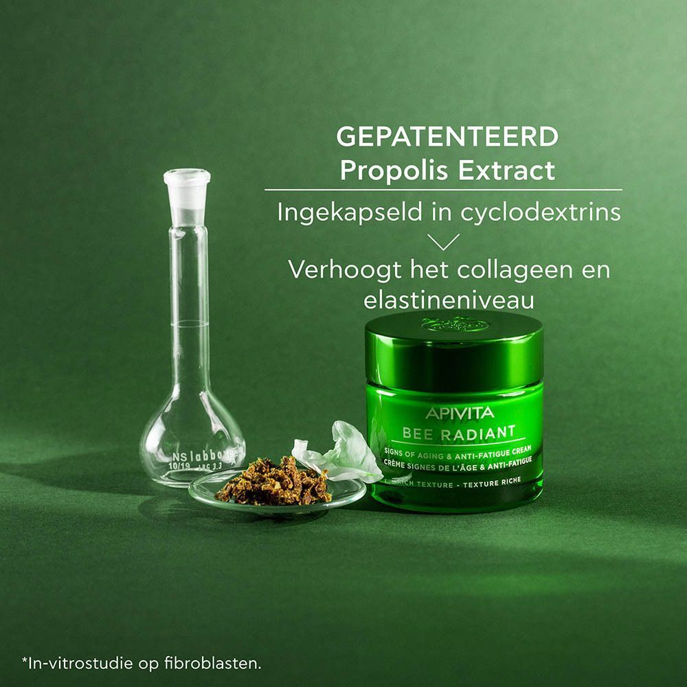 Een groen potje Apivita Bee Radiant crème naast laboratoriumapparatuur en propolis extract.