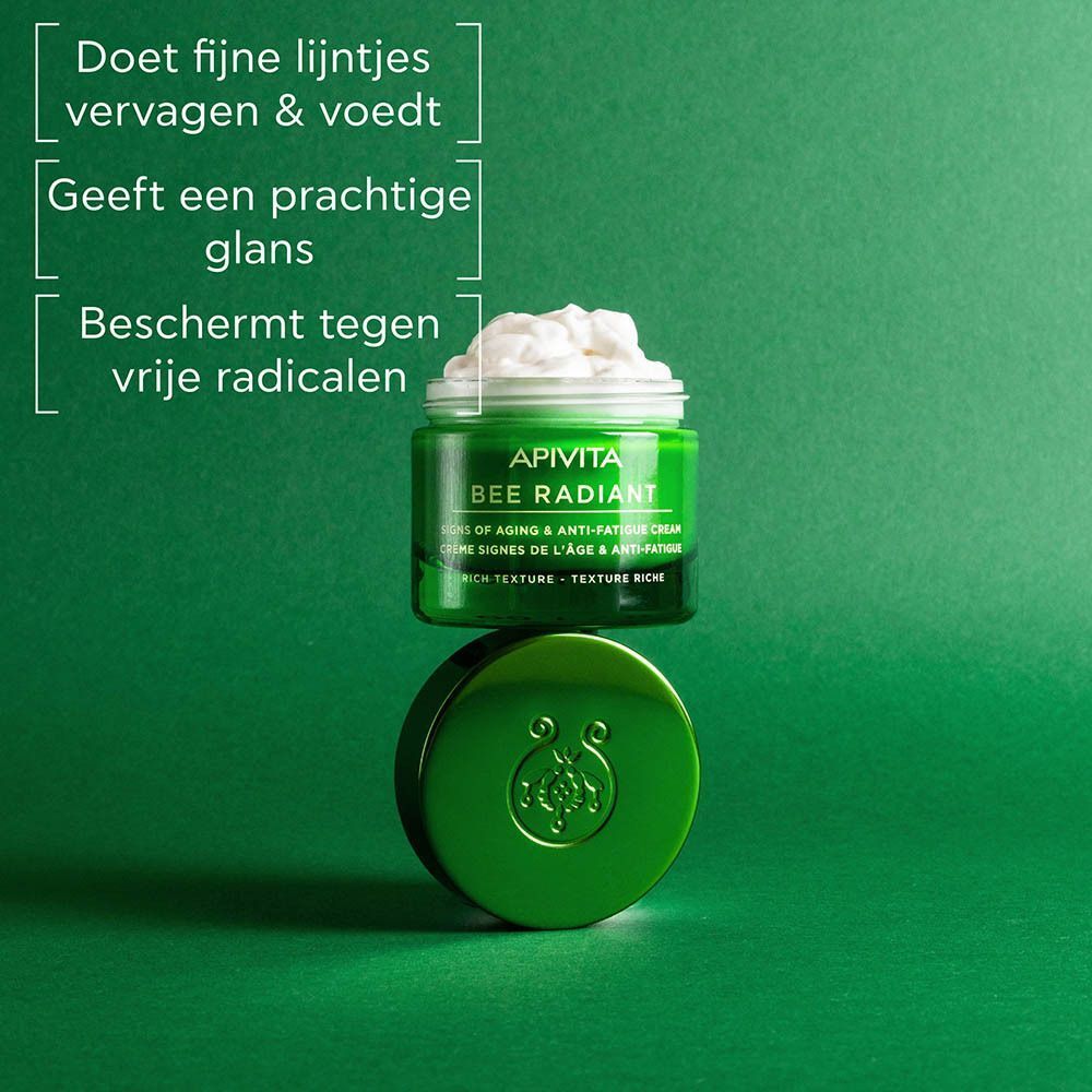 Een groen potje Apivita Bee Radiant crème met open deksel, gevuld met witte crème.