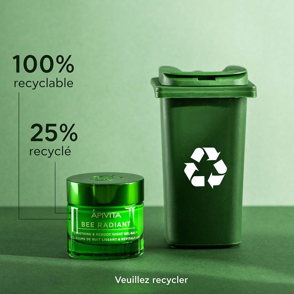 Un pot vert de crème Apivita Bee Radiant à côté d'une poubelle verte avec symbole de recyclage.