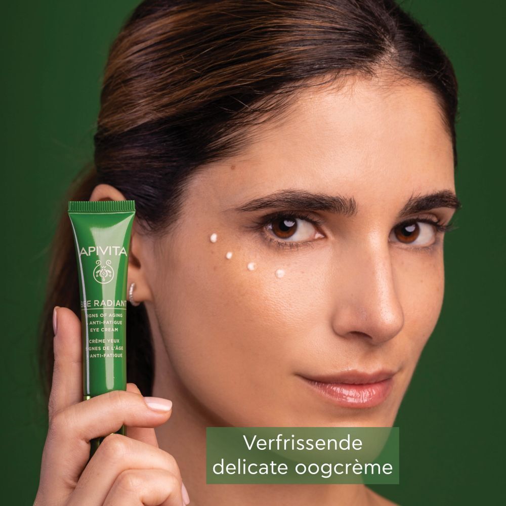 Vrouw houdt een tube Apivita Bee Radiant oogcrème vast, stipjes op de huid.
