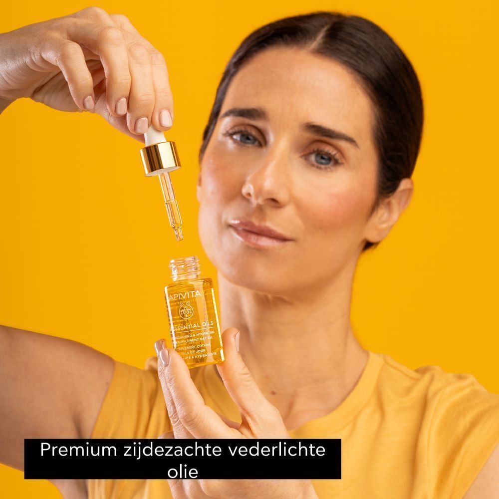 Een vrouw die een flesje Apivita Beessential Oils met druppelaar vasthoudt, terwijl er een druppel olie uitkomt.