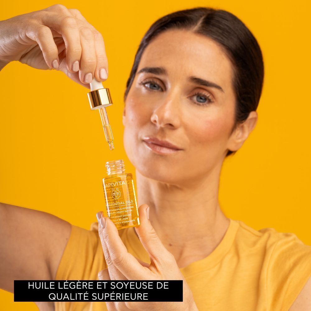 Femme tenant un flacon d'Huile de Jour Apivita avec pipette, déposant une goutte.