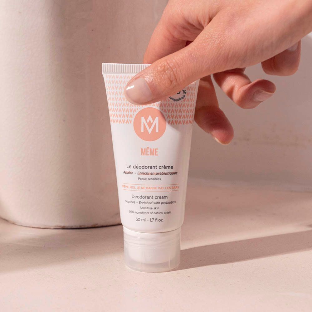 Une main tient un tube de déodorant crème MÊME.
