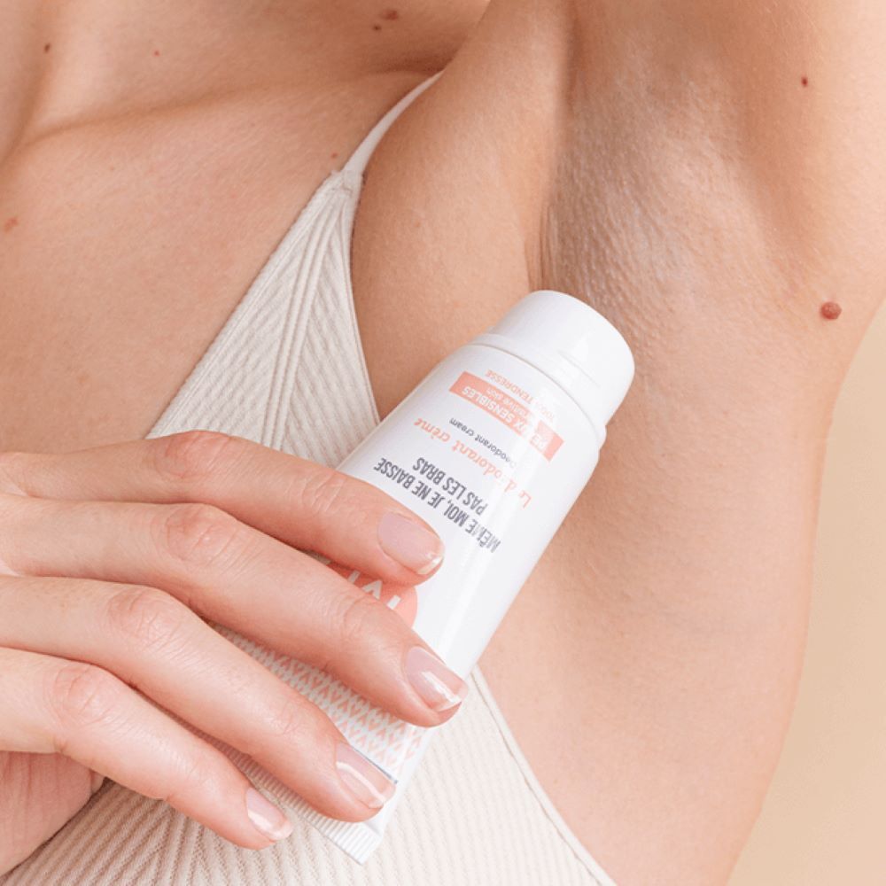 Hand houdt een tube deodorantcrème onder de oksel.