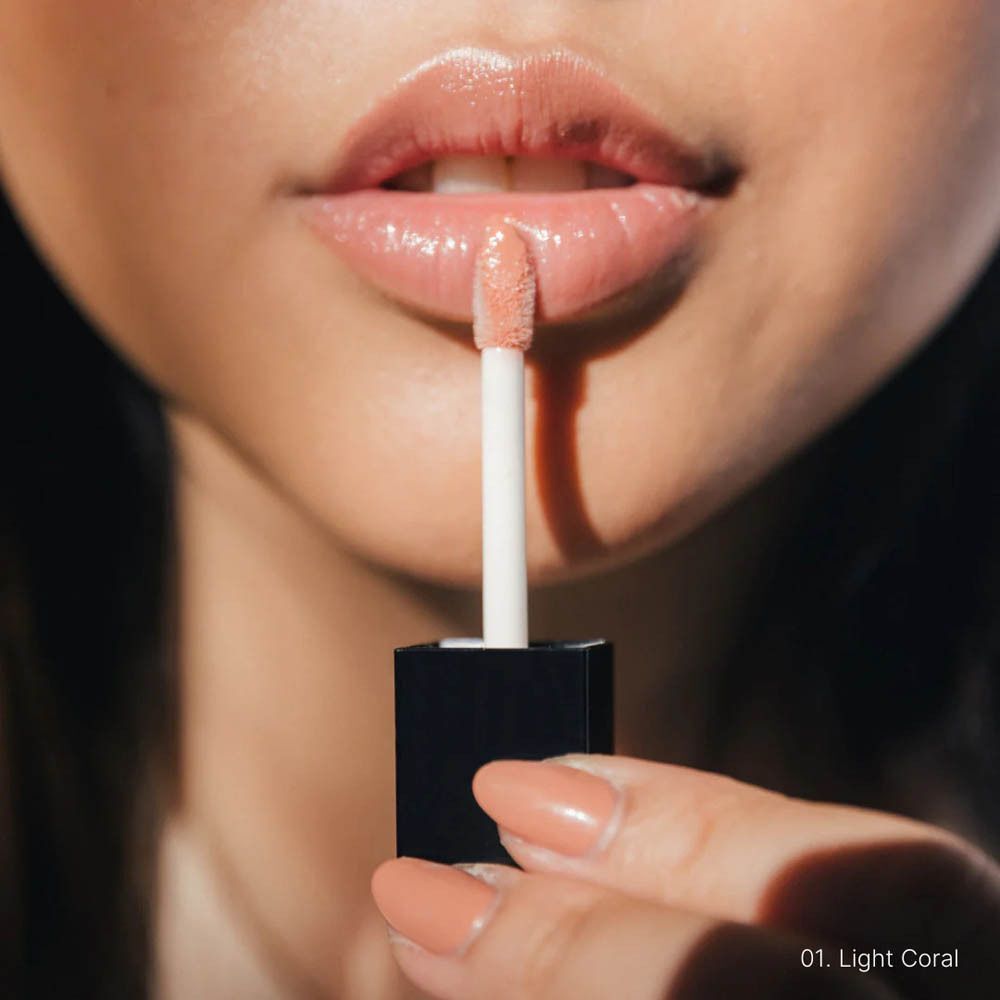 Applicateur de gloss à lèvres couleur corail clair appliqué sur les lèvres.