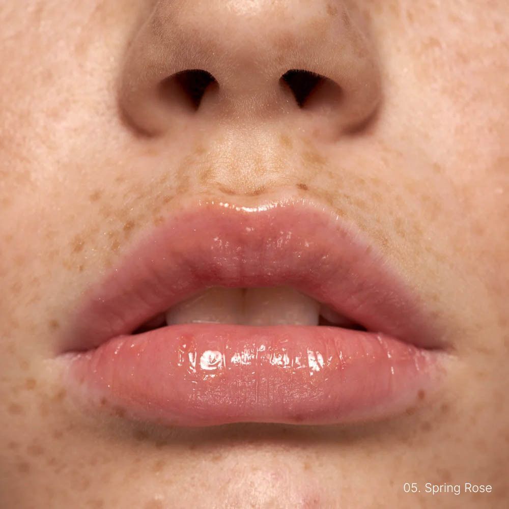 Close-up van lippen bedekt met roze lipgloss. "05 Spring Rose" staat rechtsonder vermeld.