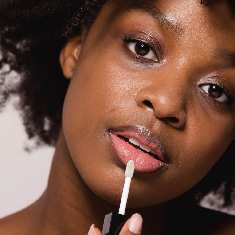 Een vrouw brengt Couleurs de Noir Instant Gloss Lip Oil aan op haar lippen met de applicator.