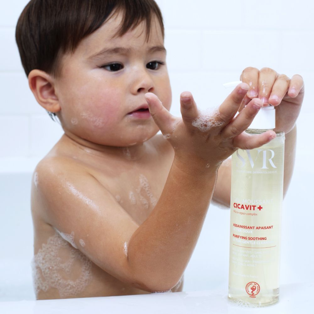 Een kind houdt een fles SVR Cicavit+ Gel Moussant vast in bad.