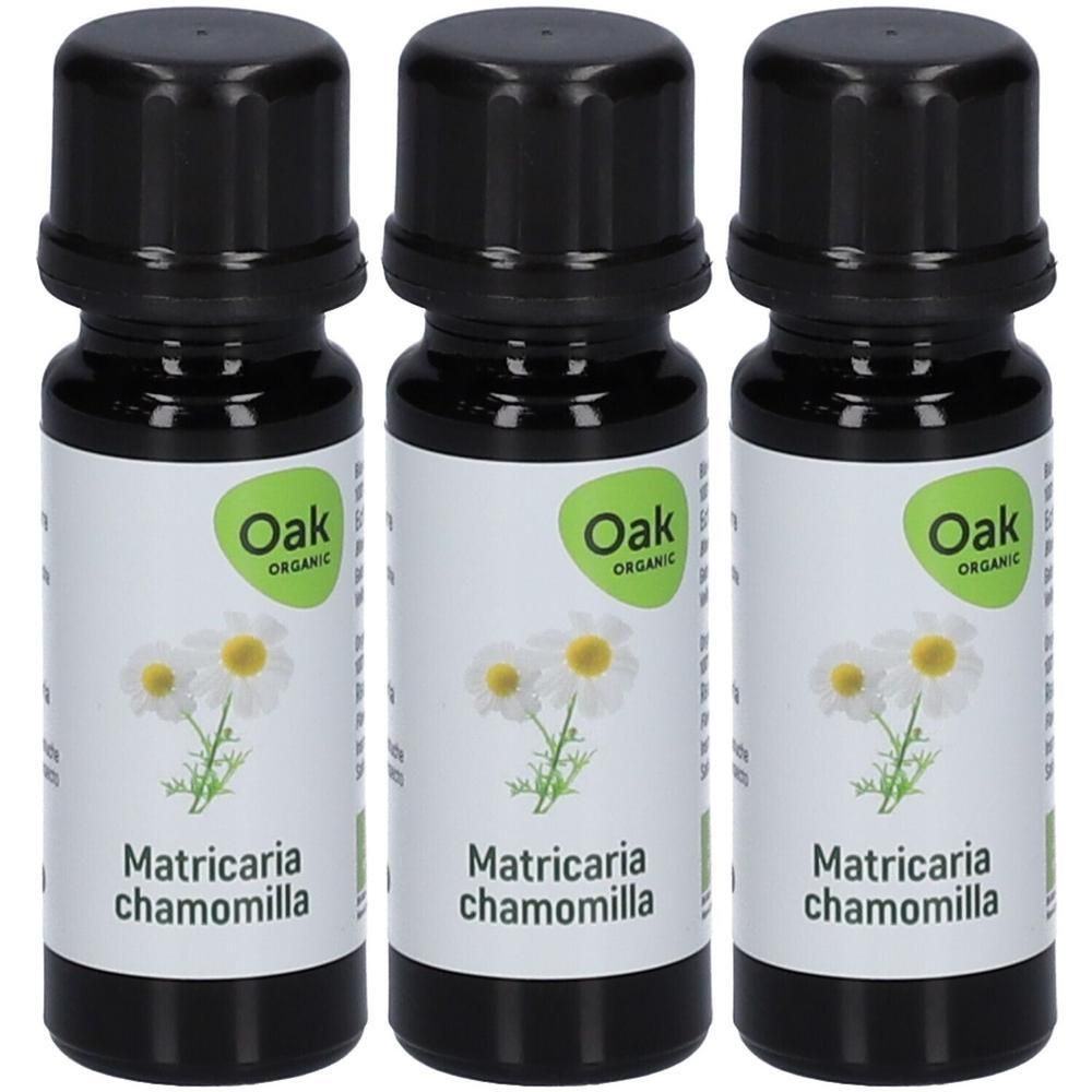 Drie flessen Oak Organic biologische kamille etherische olie met zwarte doppen en etiketten met kamillebloemen.