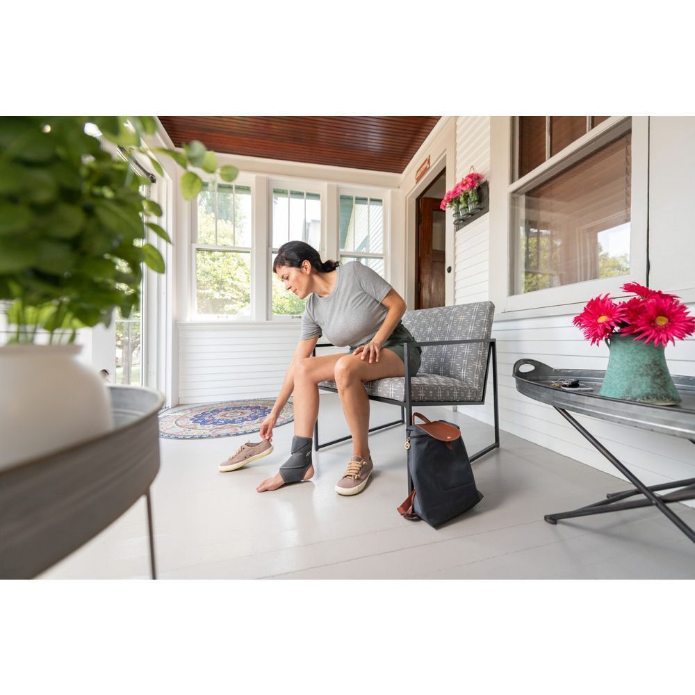 Une femme assise met une genouillère FUTURO Comfort Fit.