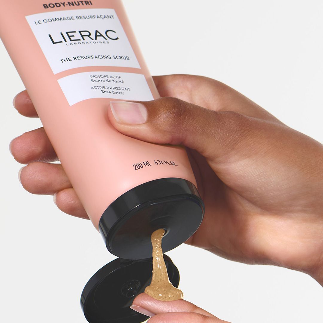 Een hand opent een tube Lierac Body-Nutri Le Gommage Resurfaçant, de scrub wordt eruit gehaald.