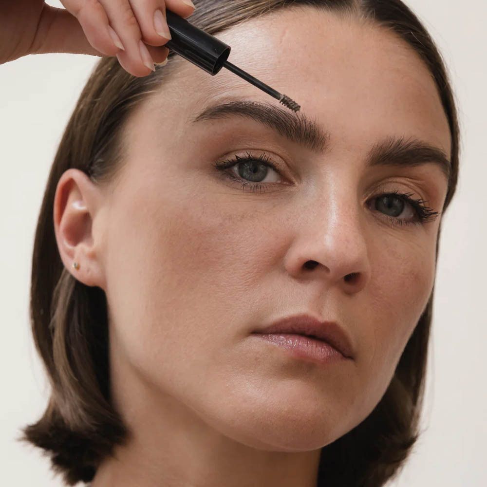 Une femme applique du sérum pour sourcils sur ses sourcils avec un applicateur.