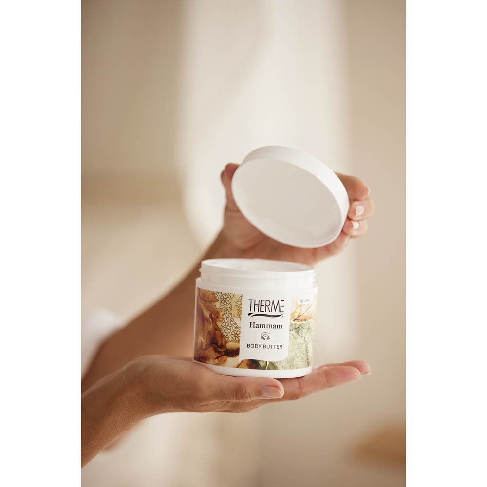 Mains tenant un pot ouvert de Beurre Corporel Therme Hammam.