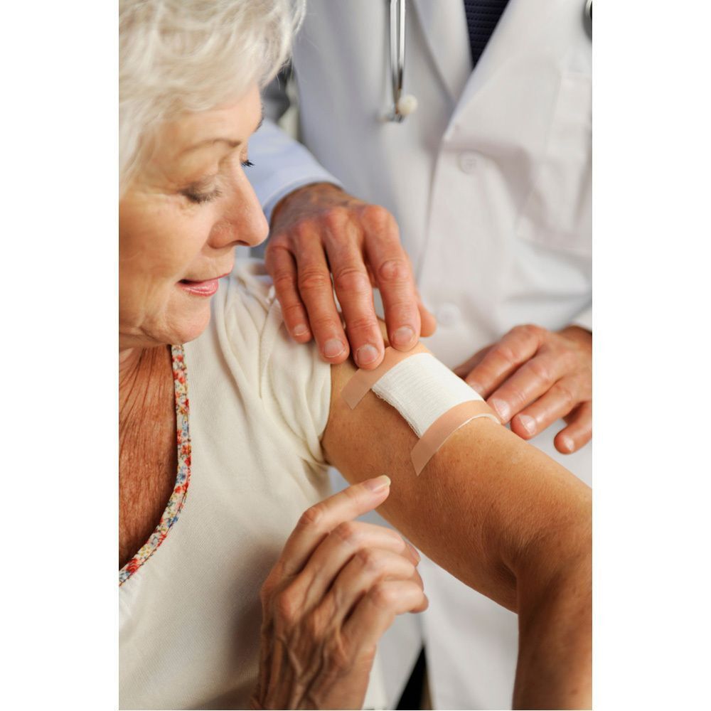 Een arts brengt een huidskleurig Nexcare textiel verband aan op de arm van een oudere vrouw.