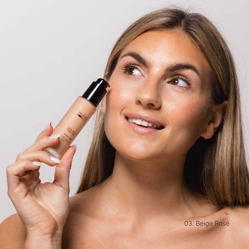 Vrouw houdt een fles COULEURS DE NOIR Fusion Glow Foundation 03 Beige Rosé vast.