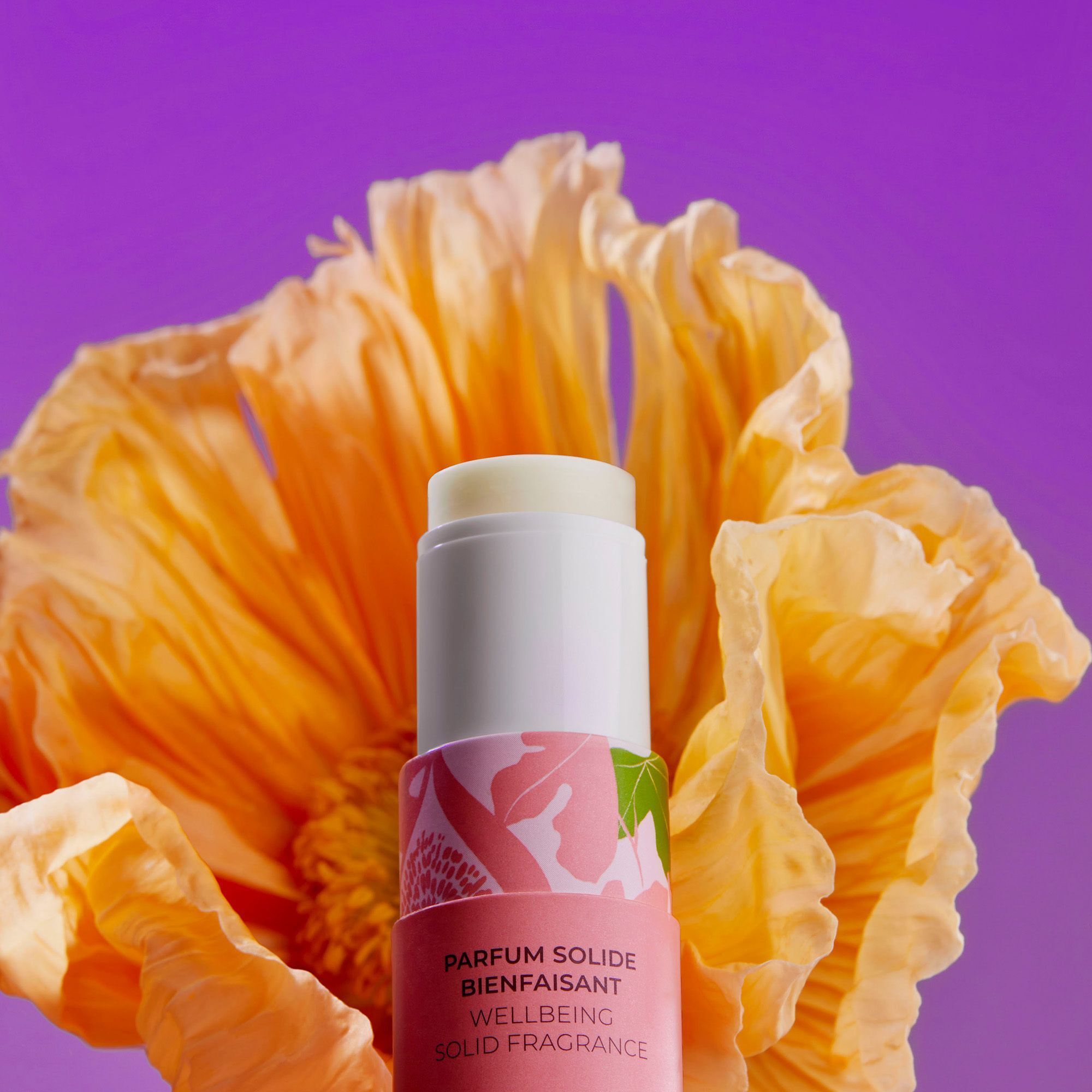 Un parfum solide Roger&Gallet en tube, entouré d'une grande fleur orange.