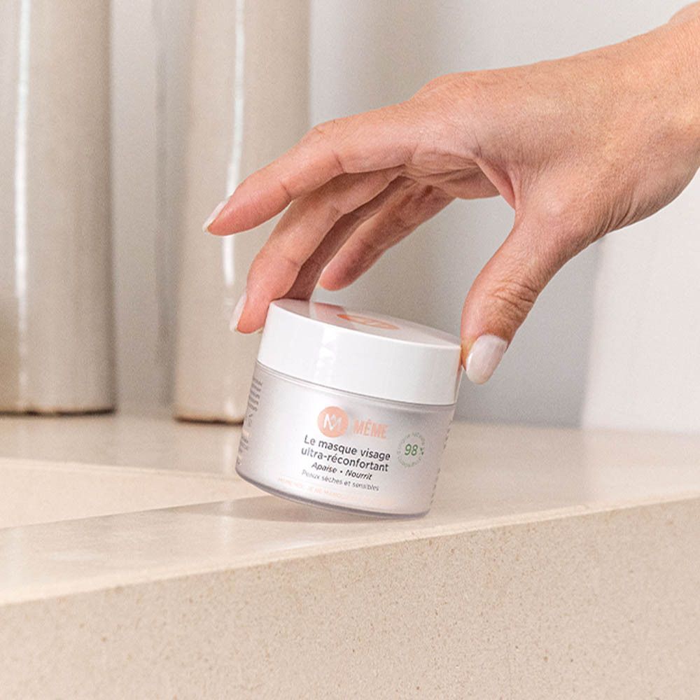 Een hand die een pot MÊME Le Masque Visage Ultra-Réconfortant vasthoudt.
