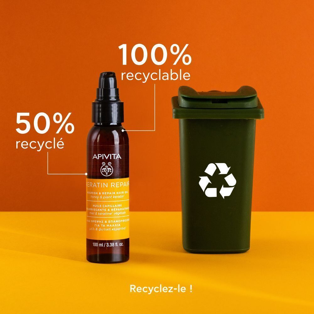 Flacon d'Huile Capillaire Apivita Keratin Repair près d'une poubelle de recyclage. 50% recyclé, 100% recyclable.