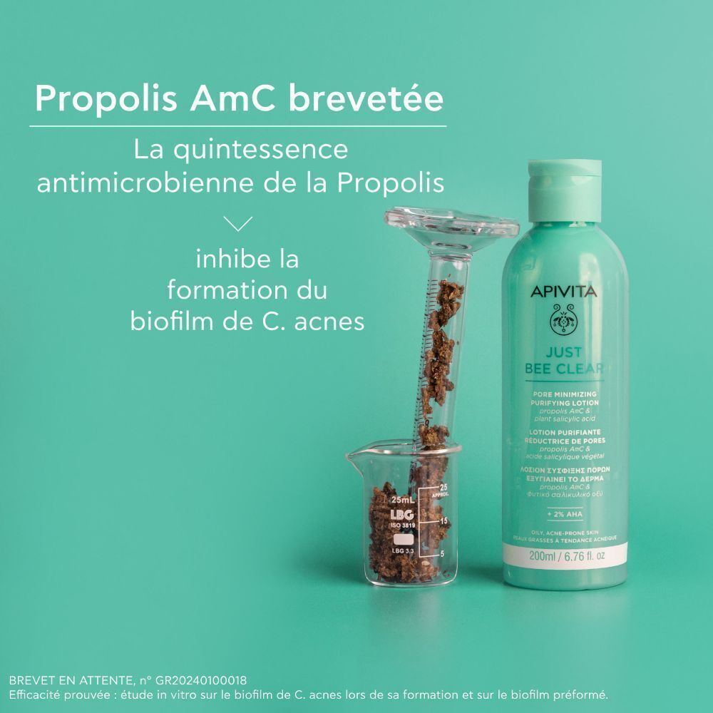 Lotion Apivita Just Bee Clear avec éprouvette et bécher contenant des extraits de propolis. Texte : 'Propolis AmC brevetée', 'inhibe la formation du biofilm de C. acnes'.