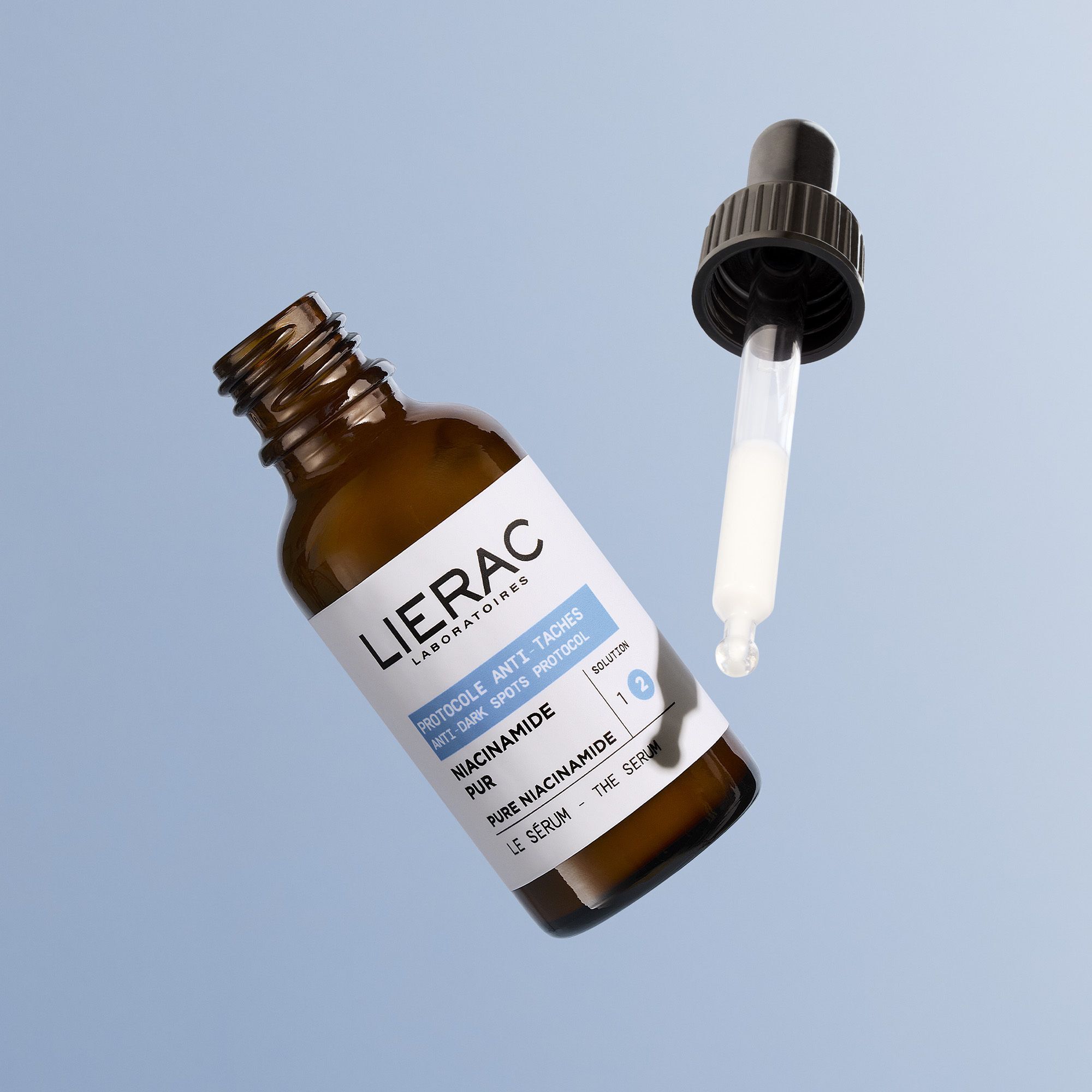 Bruin glazen flesje met druppelaar, Lierac Anti-Taches serum, op blauwe achtergrond.